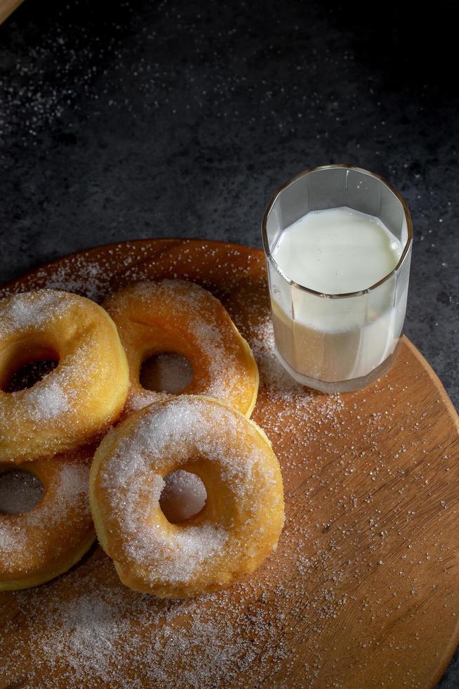 ciambelle con zucchero su un piatto di legno su uno sfondo scuro del tavolo foto