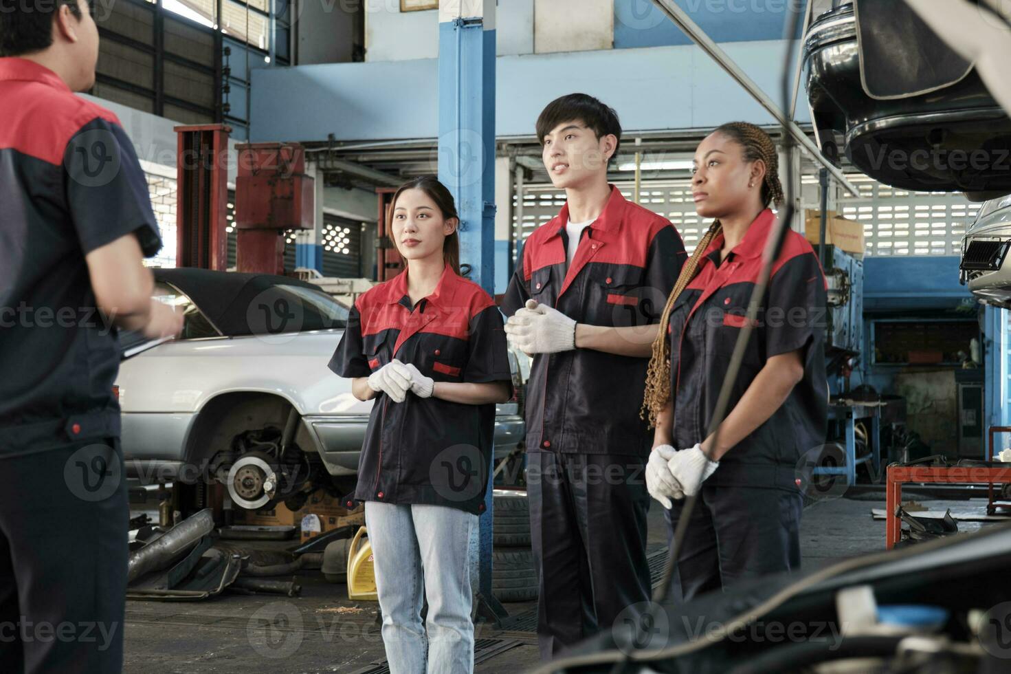 maschio esperto supervisore ingegnere treno e discutere con professionale meccanico lavoratore squadre, ispezionare riparazione opera a auto servizio box auto, armonioso gruppo, e fare Manutenzione lavori nel settore automobilistico industria. foto