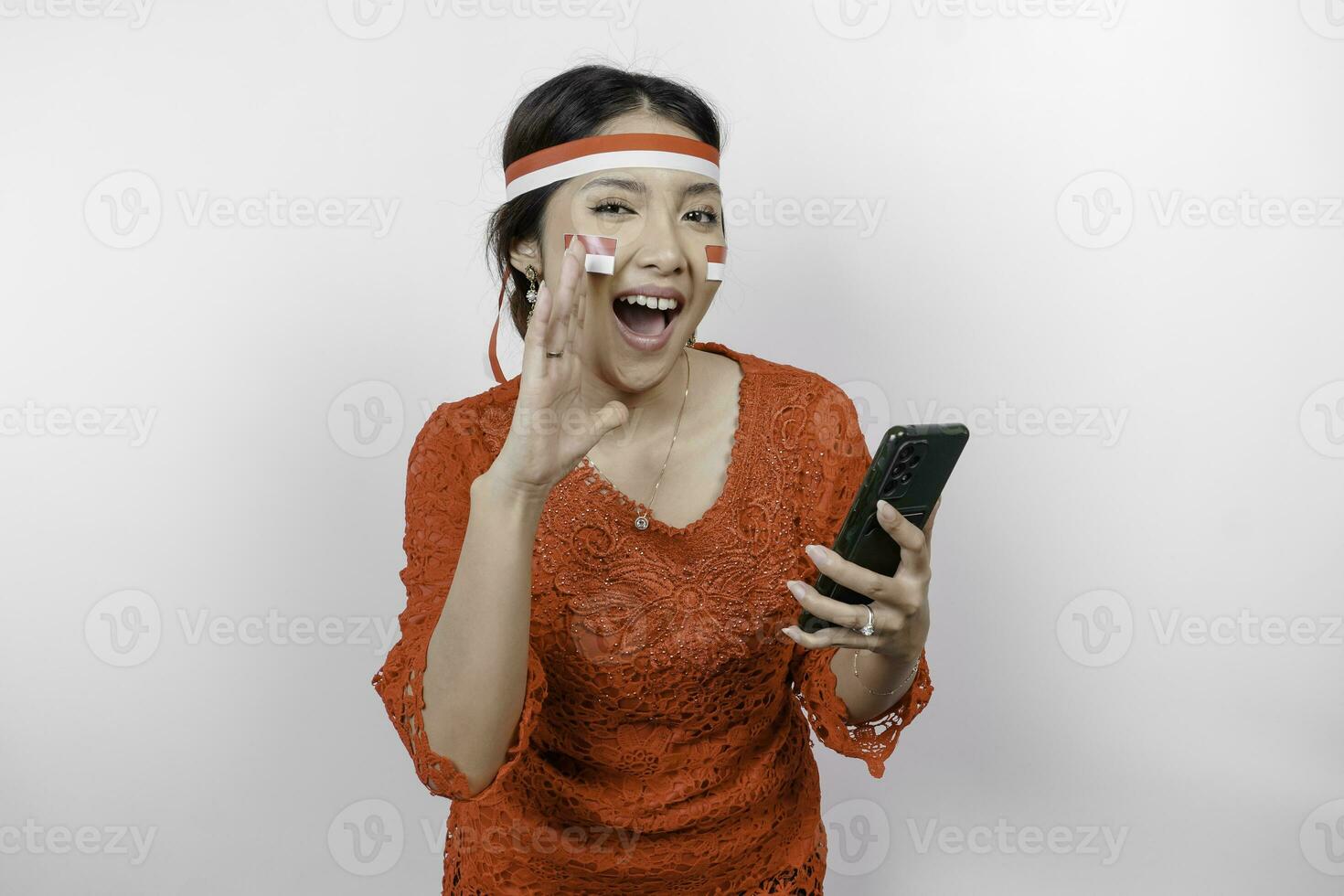 giovane bellissimo donna indossare un' rosso kebaya è Tenere sua Telefono mentre urlando e urlando forte con un' mano su sua bocca. dell'Indonesia indipendenza giorno concetto. foto