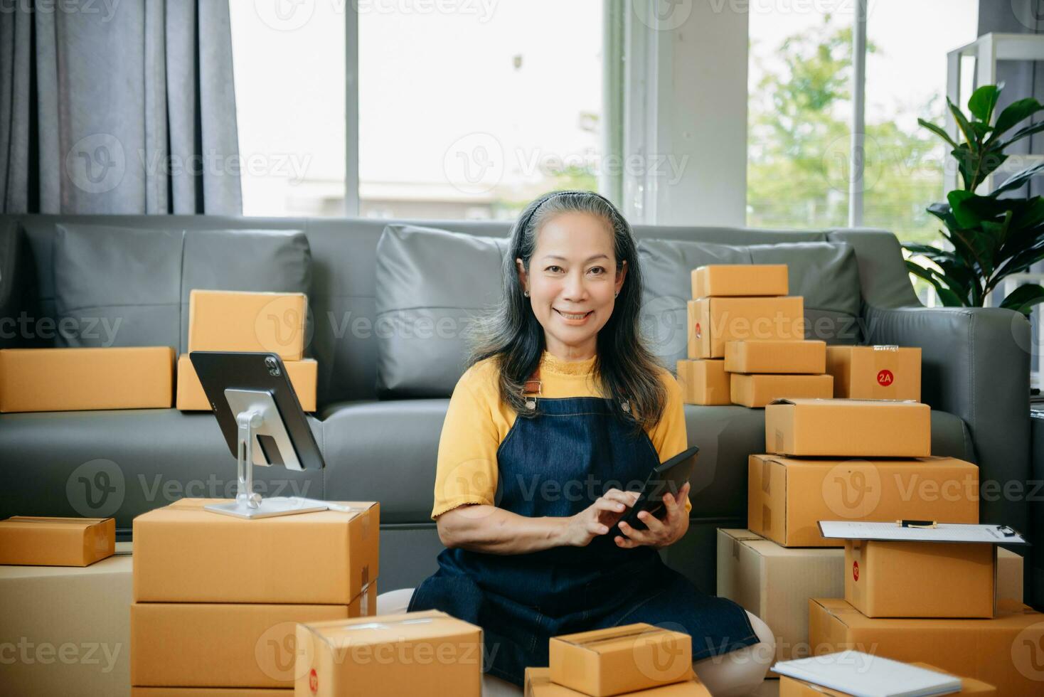 maturo attività commerciale proprietario donna preparare pacco scatola e in piedi dai un'occhiata in linea ordini per consegnare per cliente su tavoletta, il computer portatile shopping in linea foto