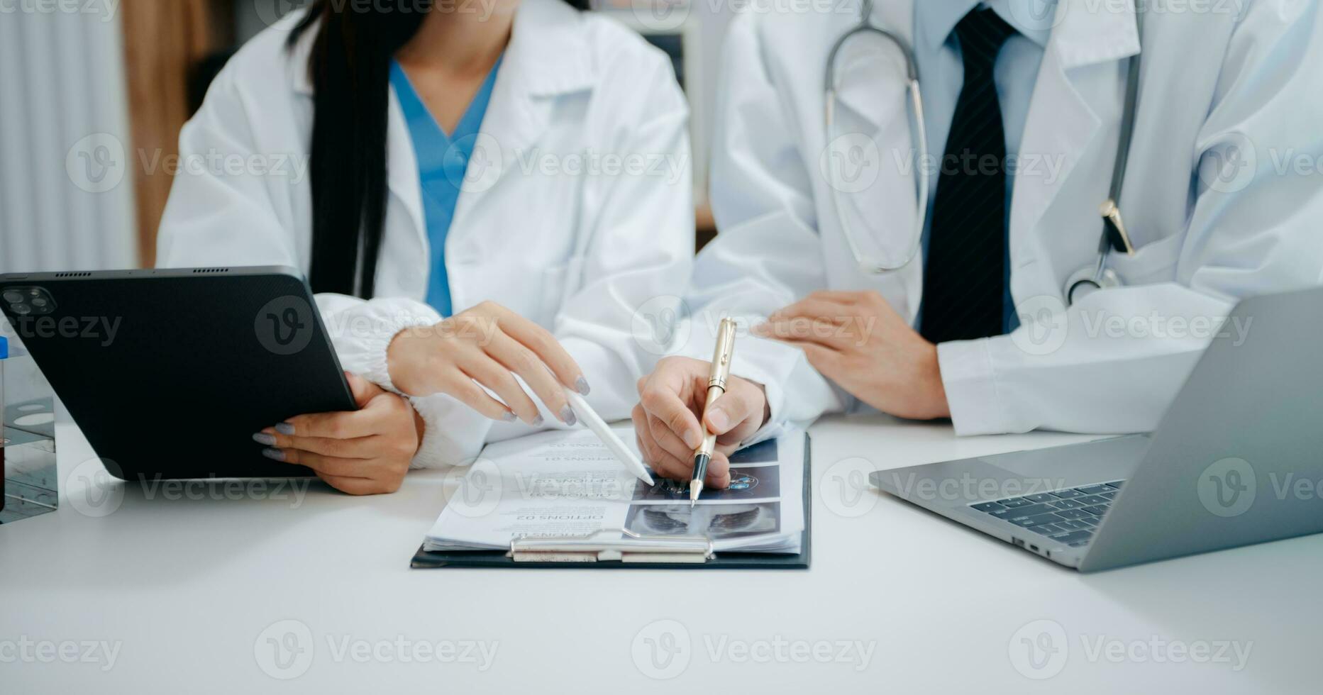 medico squadra avendo un' incontro con medici nel bianca laboratorio cappotti e chirurgico scrub seduto a un' tavolo discutere un' pazienti Lavorando in linea utilizzando computer nel il medico industria foto