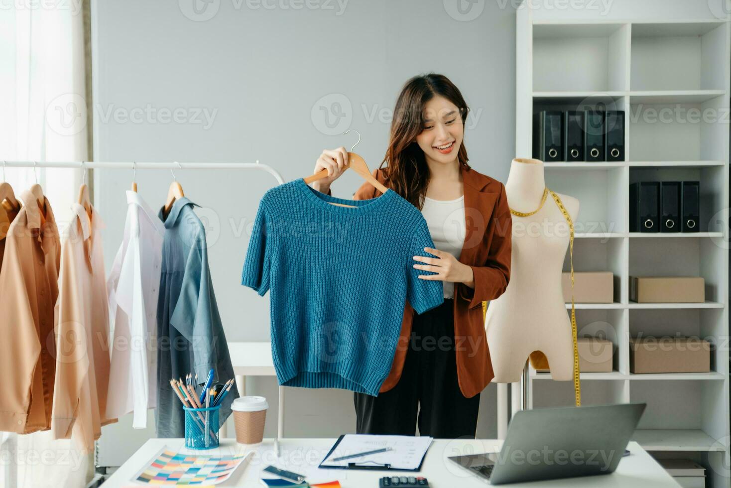 riuscito moda progettista. attraente giovane asiatico donna con Sorridi mentre in piedi nel officina. bellissimo proprietario attività commerciale donna Lavorando e detiene tavoletta, il computer portatile e smartphone nel studio. foto