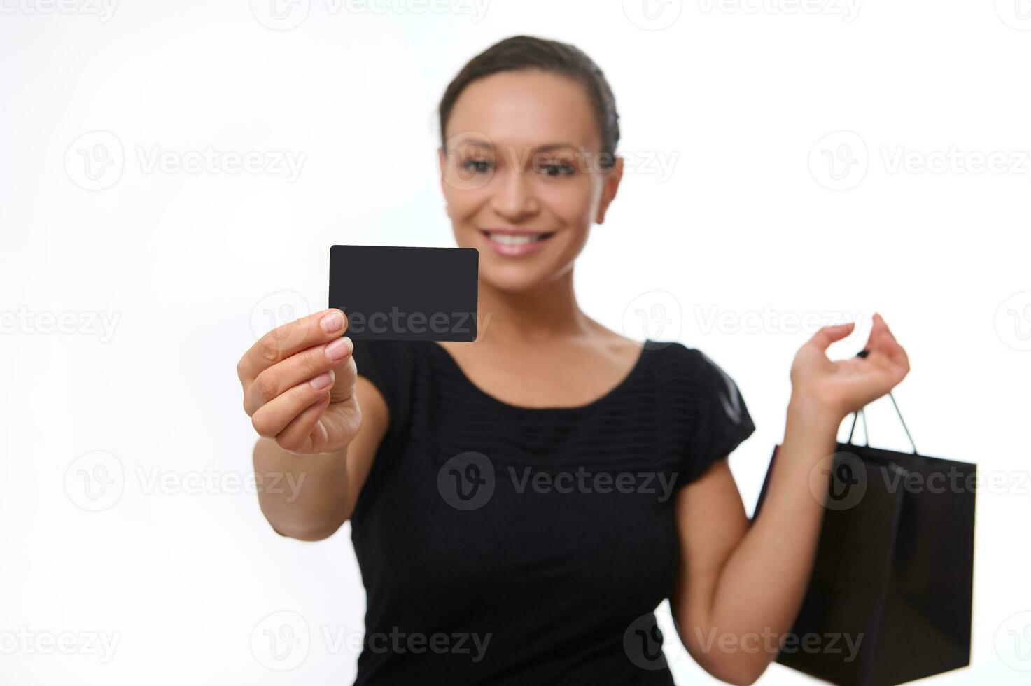 messa a fuoco su vuoto plastica nero credito sconto carta con copia spazio nel disteso mano di bellissimo sorridente donna vestito nel nero e Tenere shopping Borsa, isolato su bianca sfondo. nero Venerdì foto