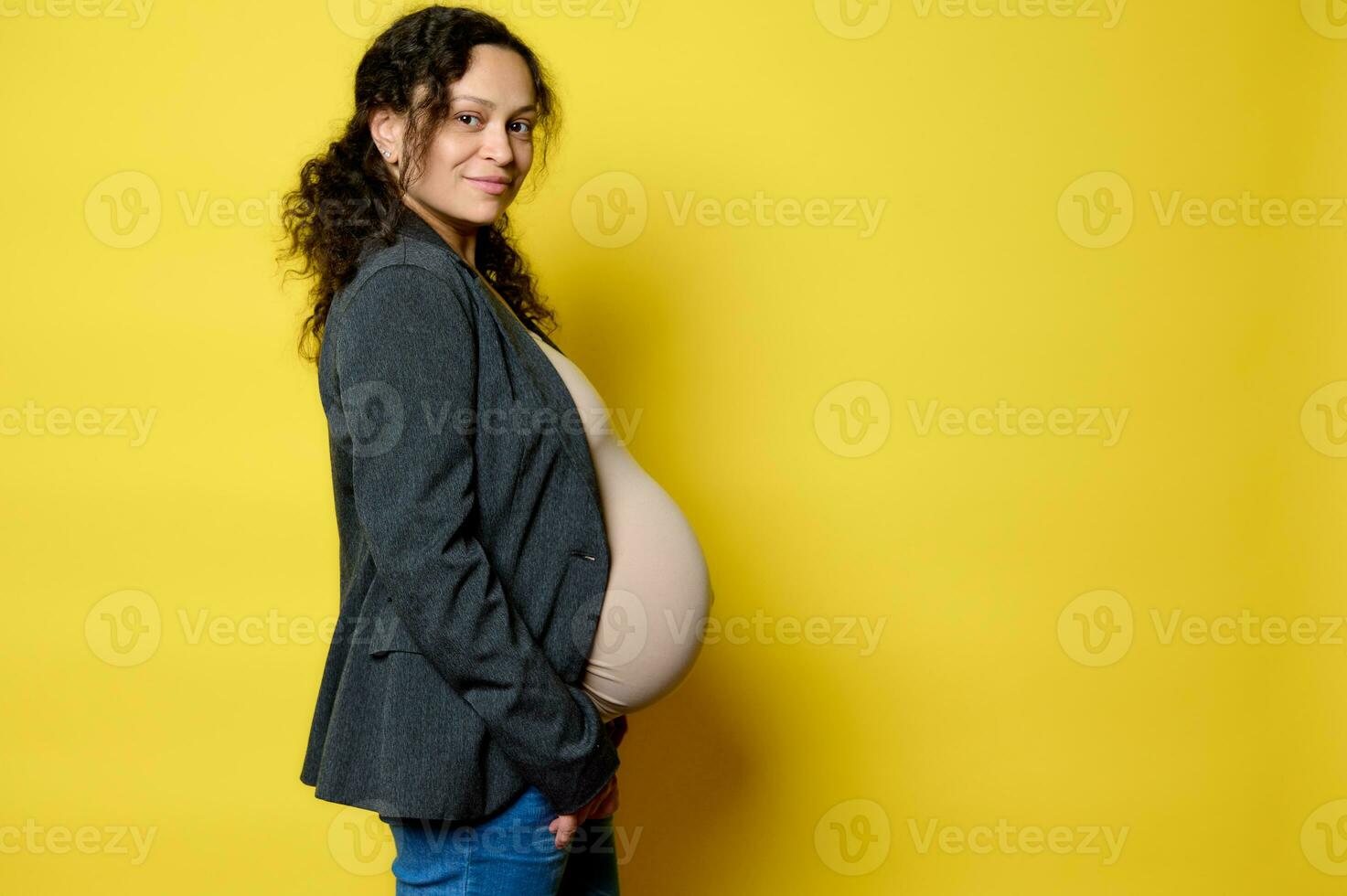 bellissimo incinta donna nel gravidanza 36 settimana, sorrisi a telecamera, si sente contento emozioni aspettandosi bambino, giallo sfondo foto