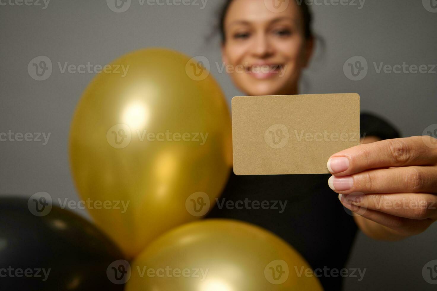 messa a fuoco su vuoto vuoto d'oro credito carta nel il mano di bellissimo sorridente bella donna Tenere nero oro aria palloncini, in posa contro grigio parete sfondo con copia spazio per anno Domini. nero Venerdì concetto foto