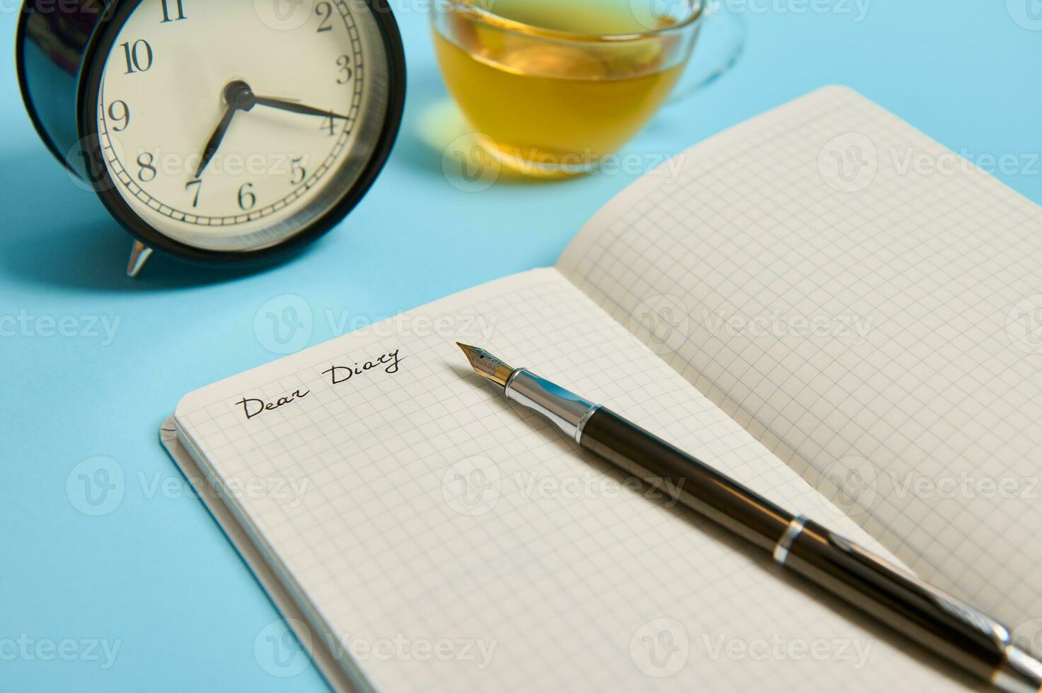 ritagliata Visualizza di un Aperto bloc notes con parola caro diario, allarme orologio e un inchiostro penna Il prossimo per un' tè tazza su blu sfondo con copia spazio foto