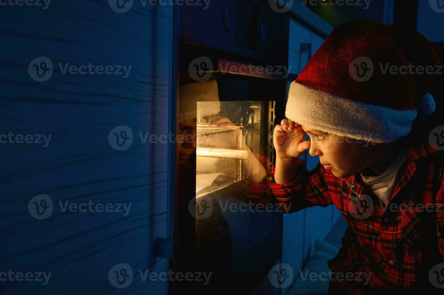 adorabile bello curioso caucasico ragazzo nel Santa cappello nel un' rosso e verde plaid camicia si siede su il pavimento e sembra attraverso il forno a il tradizionale Tedesco Stollen pane al forno su un' cottura al forno vassoio foto