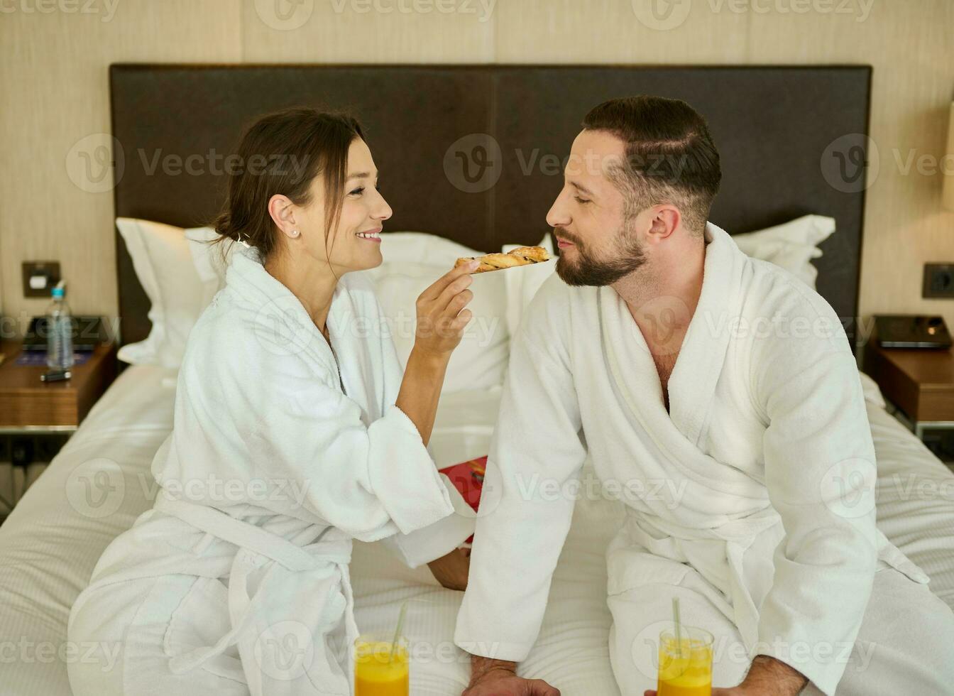 romantico mattina di giovane bellissimo coppia nel amore godendo prima colazione nel letto per Due. Novelli sposi alimentazione ogni altro delizioso pasticcini mentre avendo prima colazione nel letto nel un' Hotel camera durante loro luna di miele foto