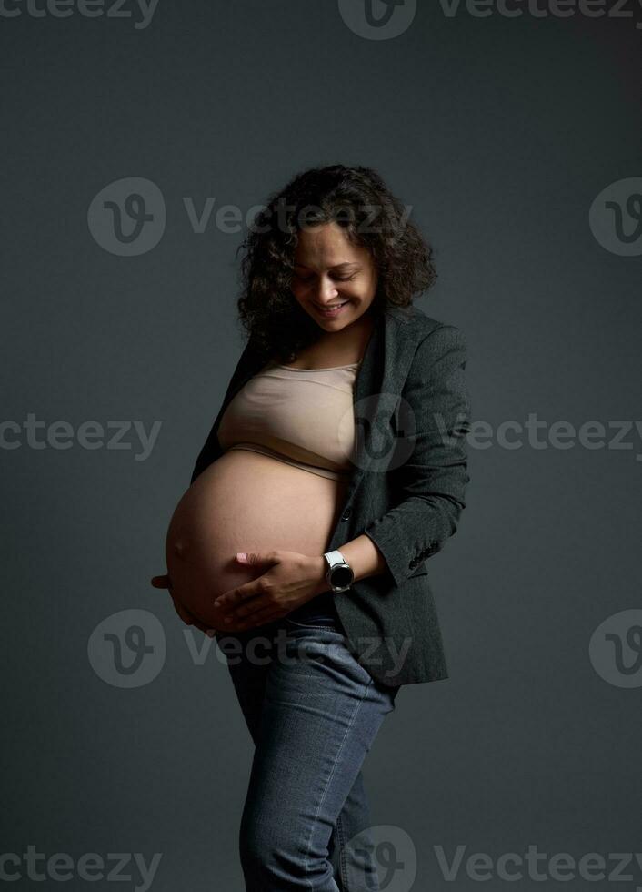 sorridente incinta donna aspettandosi bambino, tocchi gonfiarsi, sperimentare positivo emozioni sensazione bambino si sposta, grigio sfondo foto