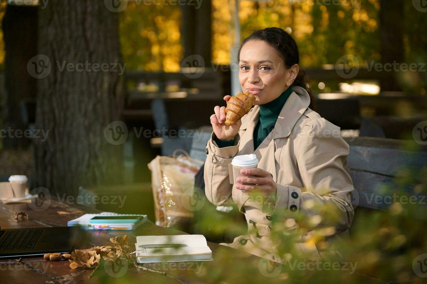 giovane fiducioso bellissimo attività commerciale donna gode sua colazione, mangia fresco brioche e bevande caffè , brividi lontano a partire dal il spingere e trambusto di il città, prima lontano opera nel accogliente all'aperto bar foto