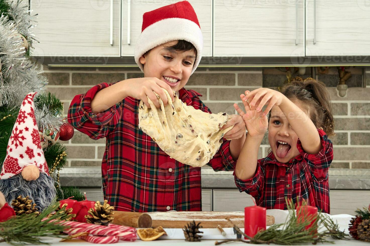 bellissimo bambini cucinando insieme nel il casa cucina durante Natale vacanze. adorabile ragazzo nel Santa cappello e il suo carino poco sorella preparazione e impasto Impasto per pane foto