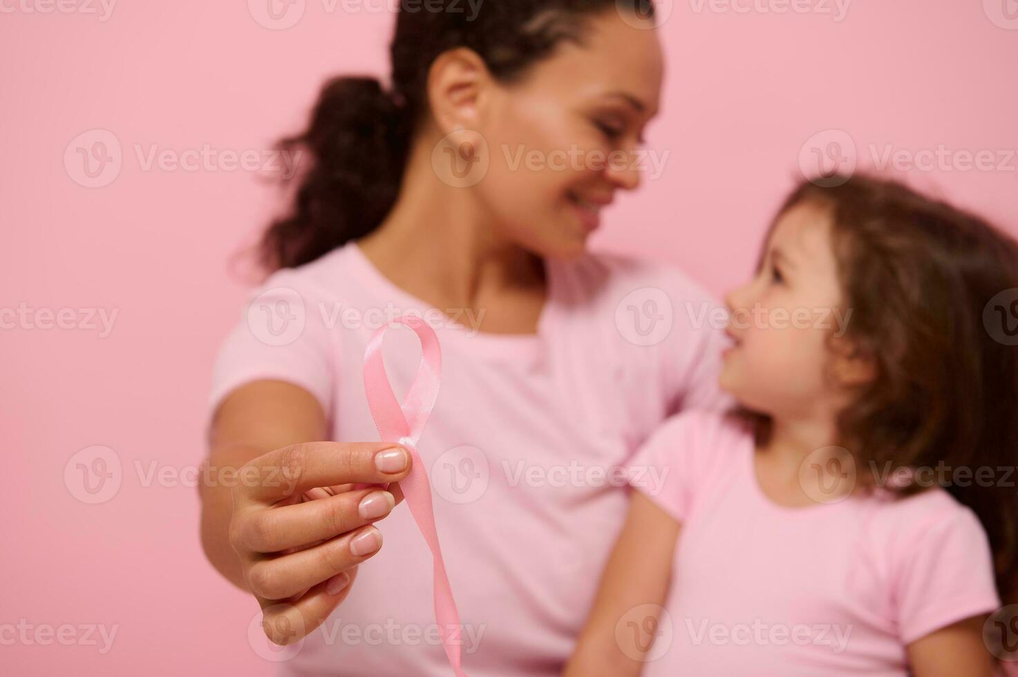 messa a fuoco su rosa nastro nel il mani di sfocato donna e ragazza indossare rosa nastri e magliette - bandiera per Seno cancro consapevolezza giorno. motivazionale slogan per combattimento cancro. medico concetto, copia spazio foto