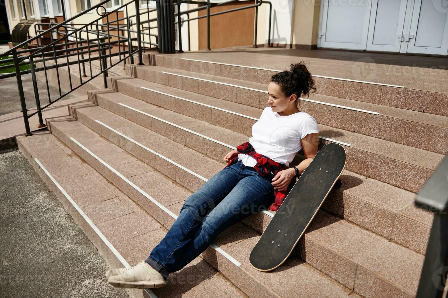 attraente africano americano donna nel casuale capi di abbigliamento in posa su le scale con skateboard e godendo soleggiato giorno foto