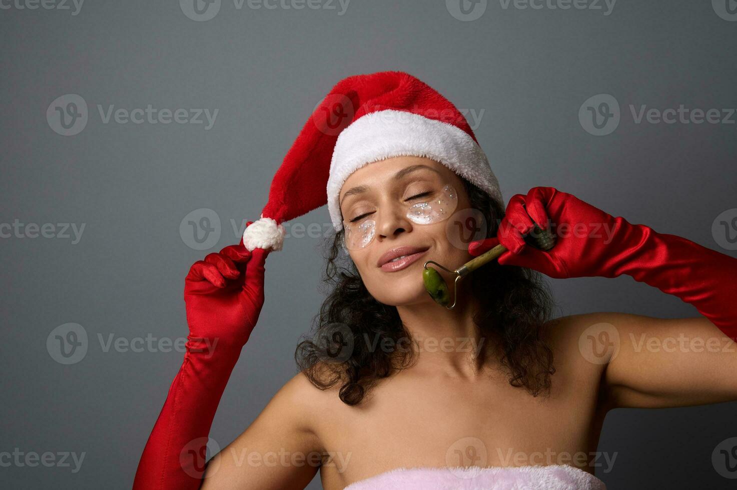 attraente donna nel Santa costume usi giada rullo massaggiatore per lifting e linfatico drenaggio facciale massaggio. pelle cura, cosmetologia concetto per Natale annuncio pubblicitario di bellezza saloni e terme foto
