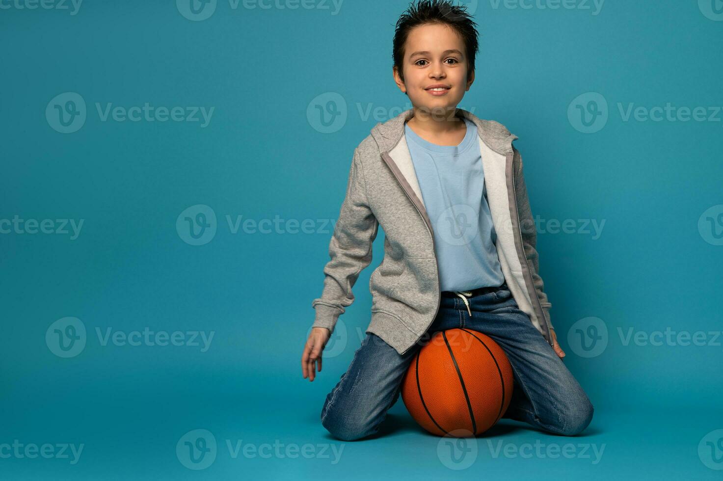 contento bambino ragazzo seduta su un' cestino palla e guardare a telecamera mentre in posa al di sopra di colore sfondo foto