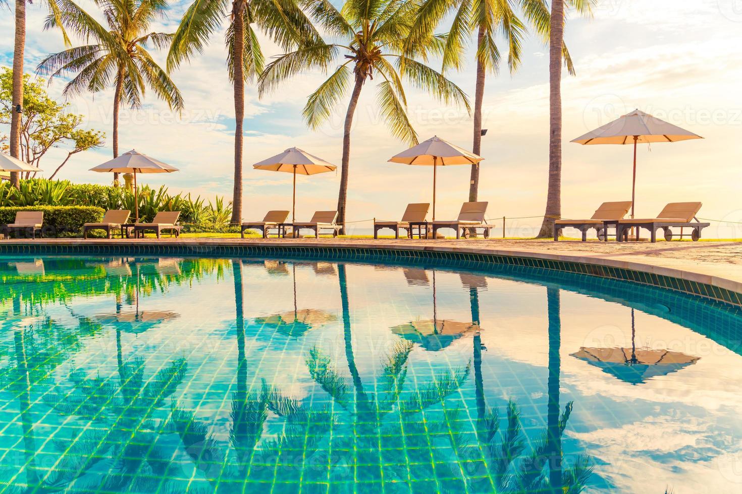 bellissimo ombrellone di lusso e sedia intorno alla piscina all'aperto in hotel e resort con palme da cocco al tramonto o all'alba sky foto