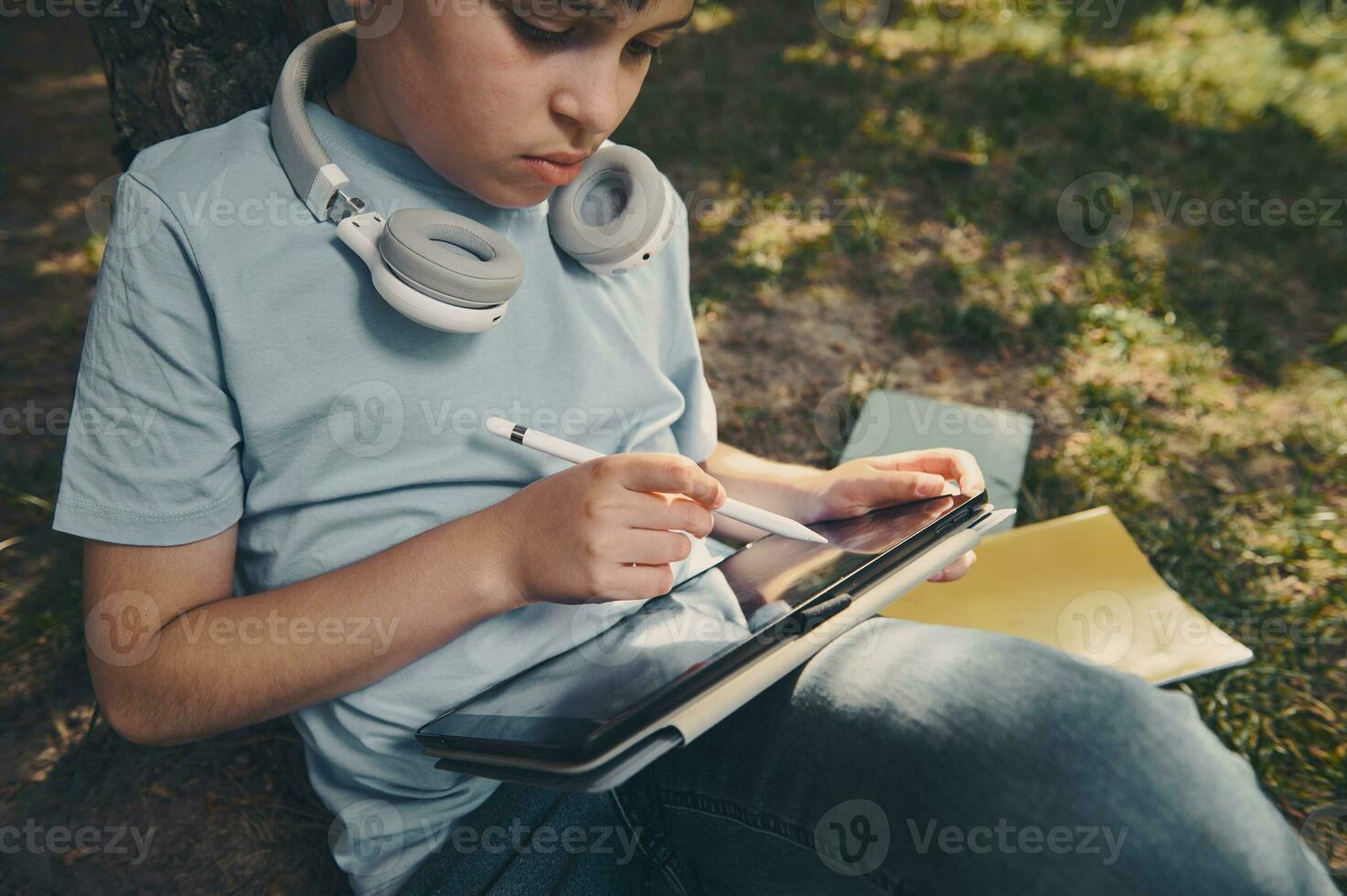 bello inteligente scuola ragazzo utilizzando un' digitale tavoletta e stilo penna, disegno, schizzi, godendo il suo creativo passatempo all'aperto foto