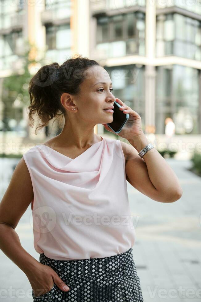 giovane africano americano misto gara donna parlando su mobile Telefono su il urbano sfondo foto