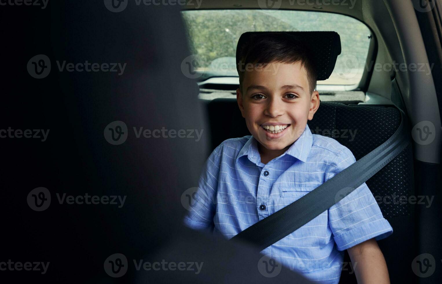 tiro attraverso il autista posto a sedere di un' sorridente ragazzo fissato con cintura di sicurezza mentre in viaggio di auto nel sicurezza bambino auto posto a sedere foto