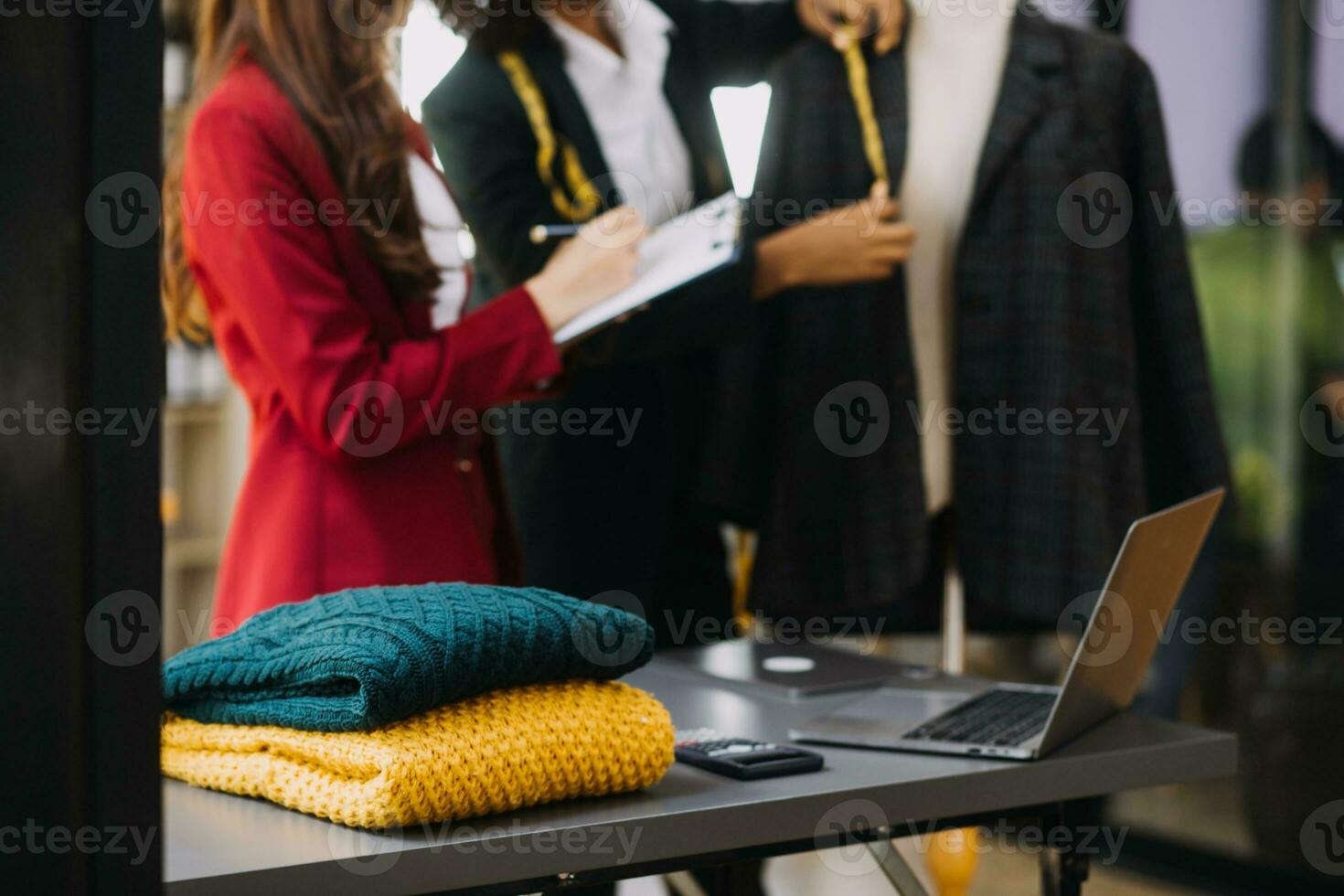 femmina moda, progettista, guardare a disegni e schizzi quello siamo appuntato per il parete dietro a sua scrivania. studio è soleggiato. personale computer, colorato tessuti, cucire elementi siamo visibile. foto