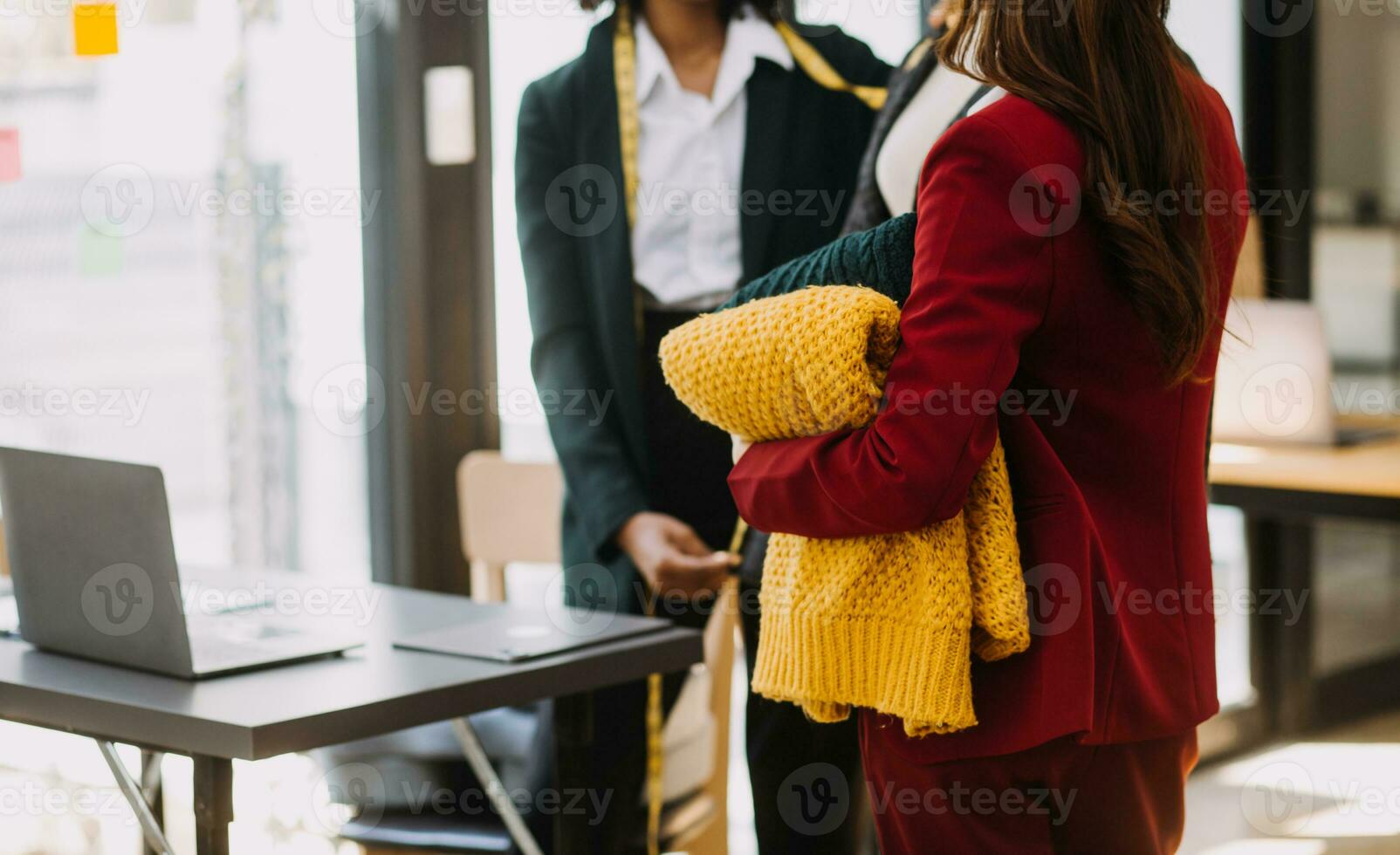 femmina moda, progettista, guardare a disegni e schizzi quello siamo appuntato per il parete dietro a sua scrivania. studio è soleggiato. personale computer, colorato tessuti, cucire elementi siamo visibile. foto