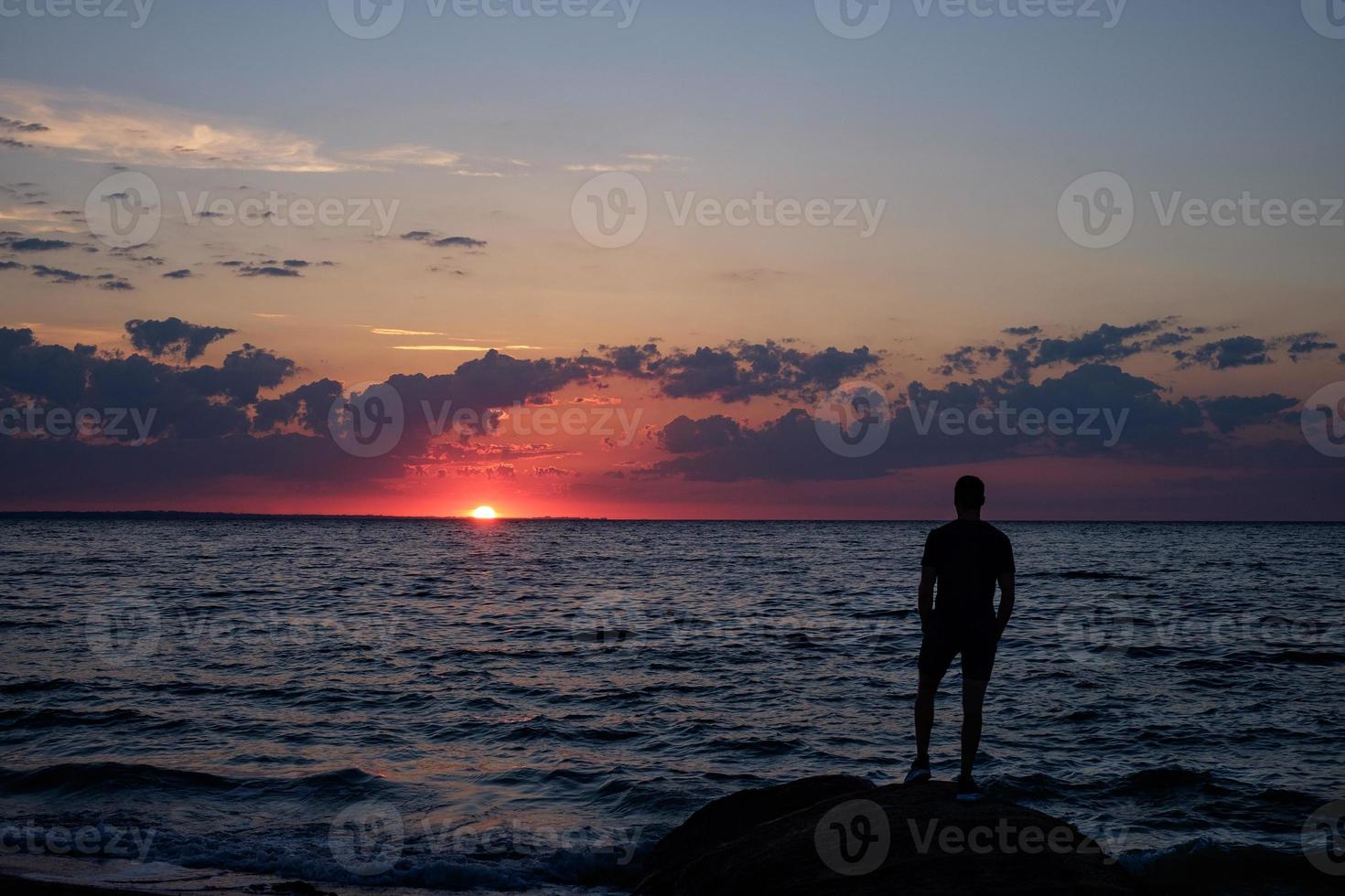 uomo in piedi su una roccia in riva al mare e guardando l'alba foto