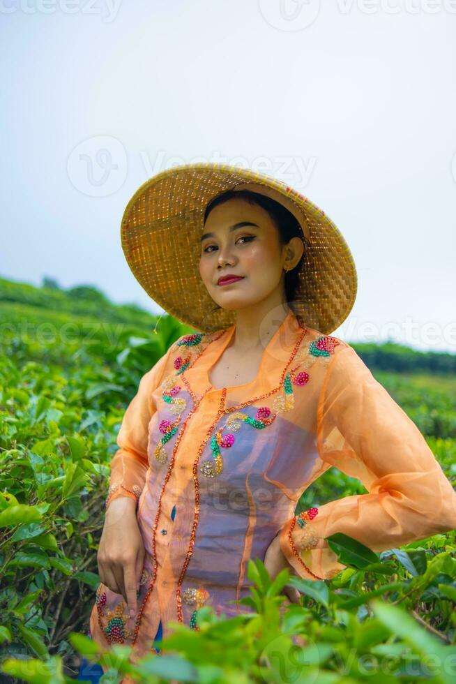 un' giavanese donna è guardare dopo sua tè giardino quando lei indossa un arancia vestito foto