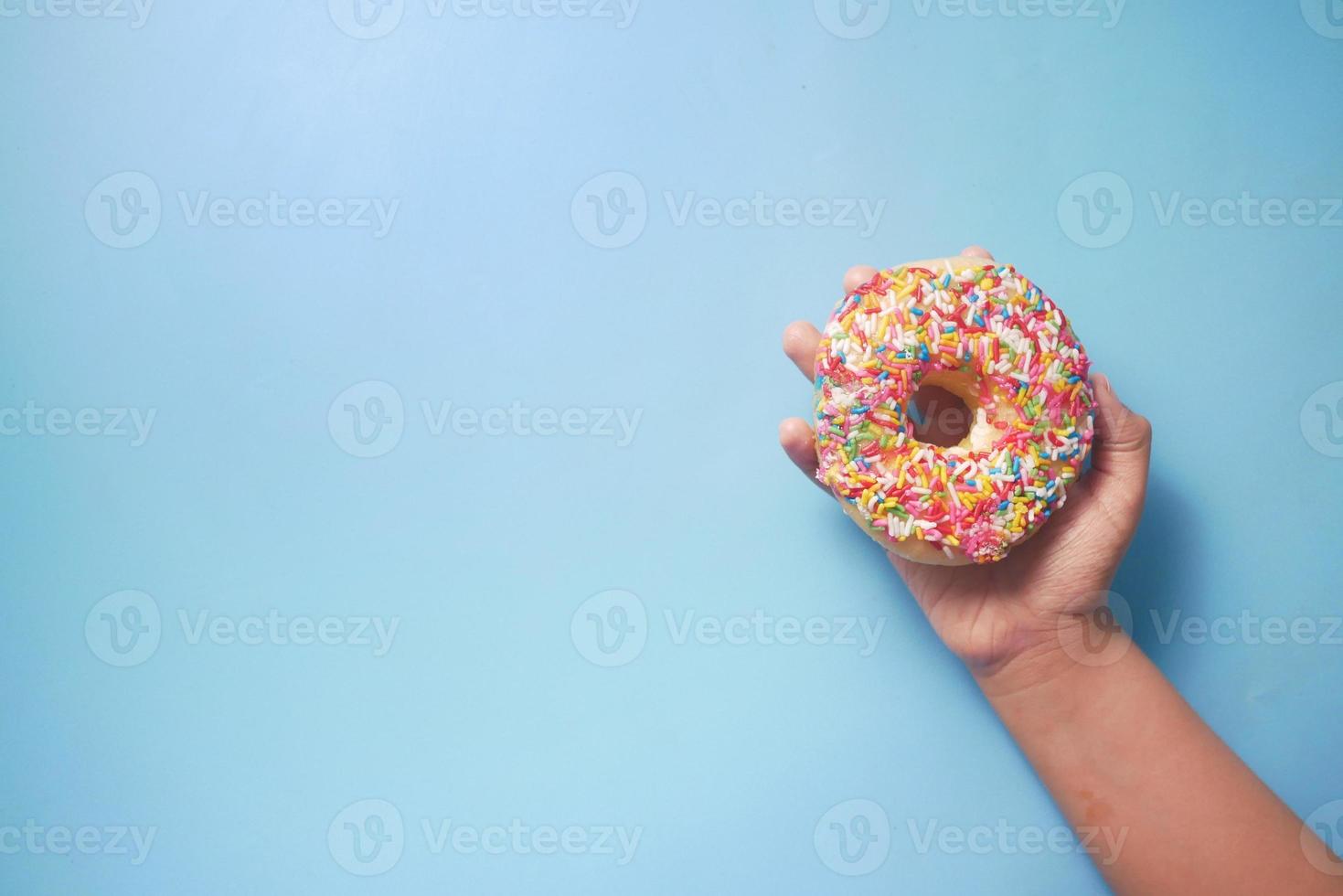 mano del bambino che tiene ciambelle fresche su sfondo blu foto