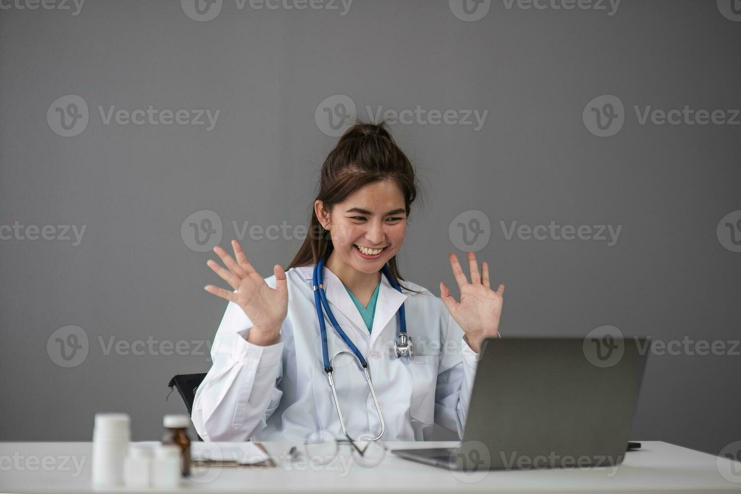 giovane dottoressa asiatica in uniforme medica bianca con stetoscopio utilizzando il computer portatile parlando in videoconferenza con il paziente alla scrivania in clinica o ospedale. concetto di consulenza e terapia. foto