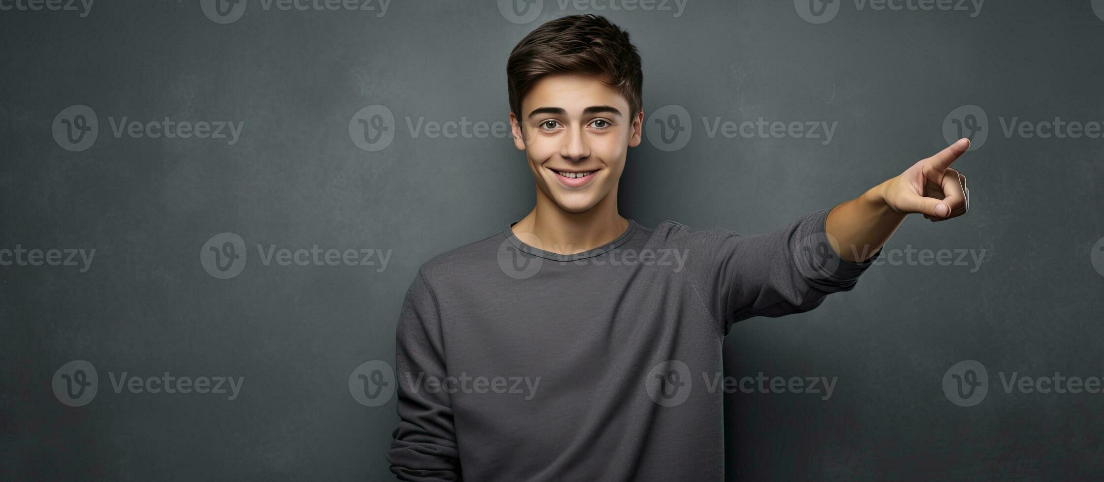 sorridente adolescenziale ragazzo puntamento verso l'alto nel un' ritratto su un' grigio sfondo foto
