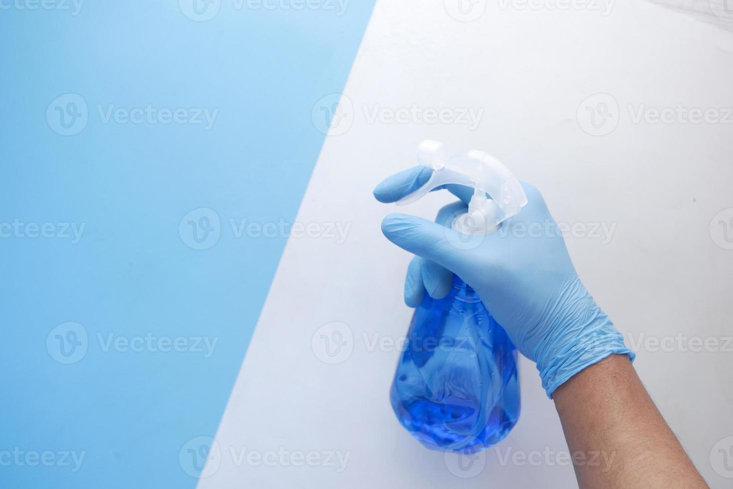 mano in guanti di gomma blu che tengono il flacone spray con copia spazio foto