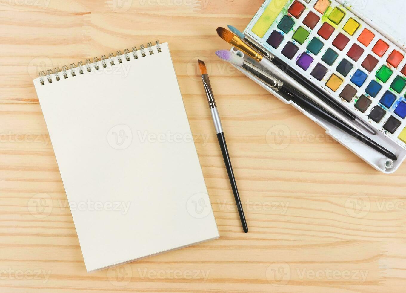 piatto posare di artista spazio di lavoro. vuoto carta, disegno Strumenti, stazionario forniture, acquerello vernici e spazzole e disegno libro su di legno tavolo, copia spazio. foto