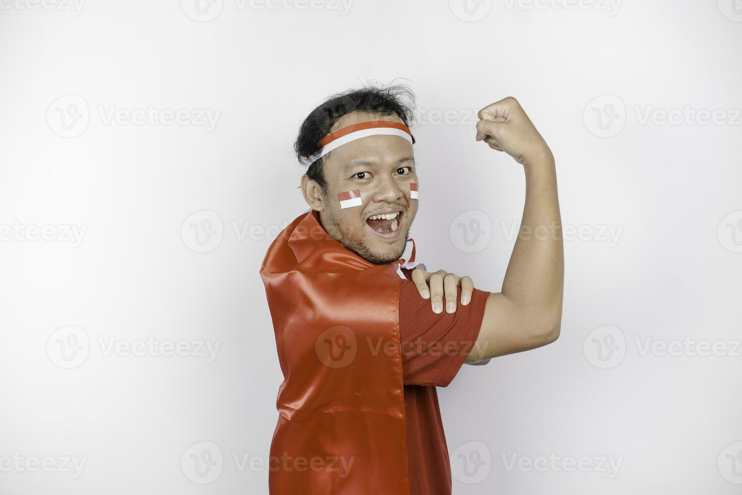 eccitato asiatico uomo indossare un' rosso superiore, bandiera capo e fascia per capelli, mostrando forte gesto di sollevamento il suo braccia e muscoli sorridente con orgoglio. dell'Indonesia indipendenza giorno concetto. foto