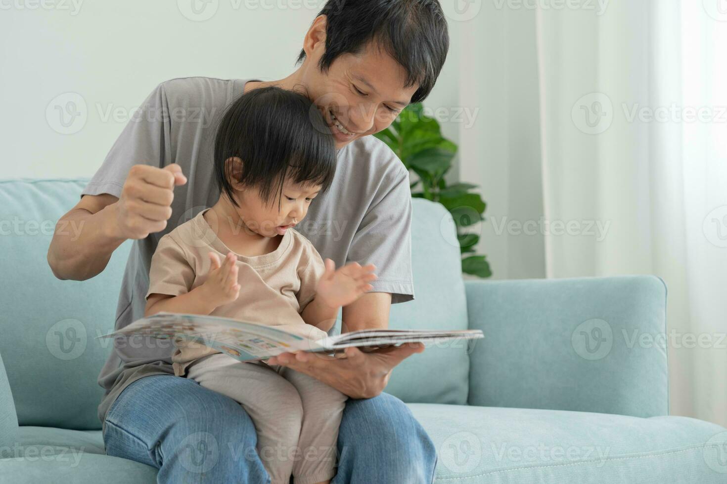 contento asiatico padre rilassare e leggere libro con bambino tempo insieme a casa. genitore sedersi su divano con figlia e lettura un' storia. imparare sviluppo, assistenza all'infanzia, ridendo, formazione scolastica, narrativa, la pratica. foto