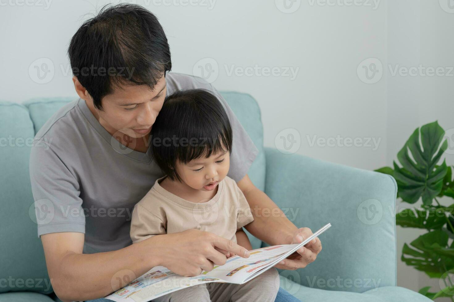 contento asiatico padre rilassare e leggere libro con bambino tempo insieme a casa. genitore sedersi su divano con figlia e lettura un' storia. imparare sviluppo, assistenza all'infanzia, ridendo, formazione scolastica, narrativa, la pratica. foto