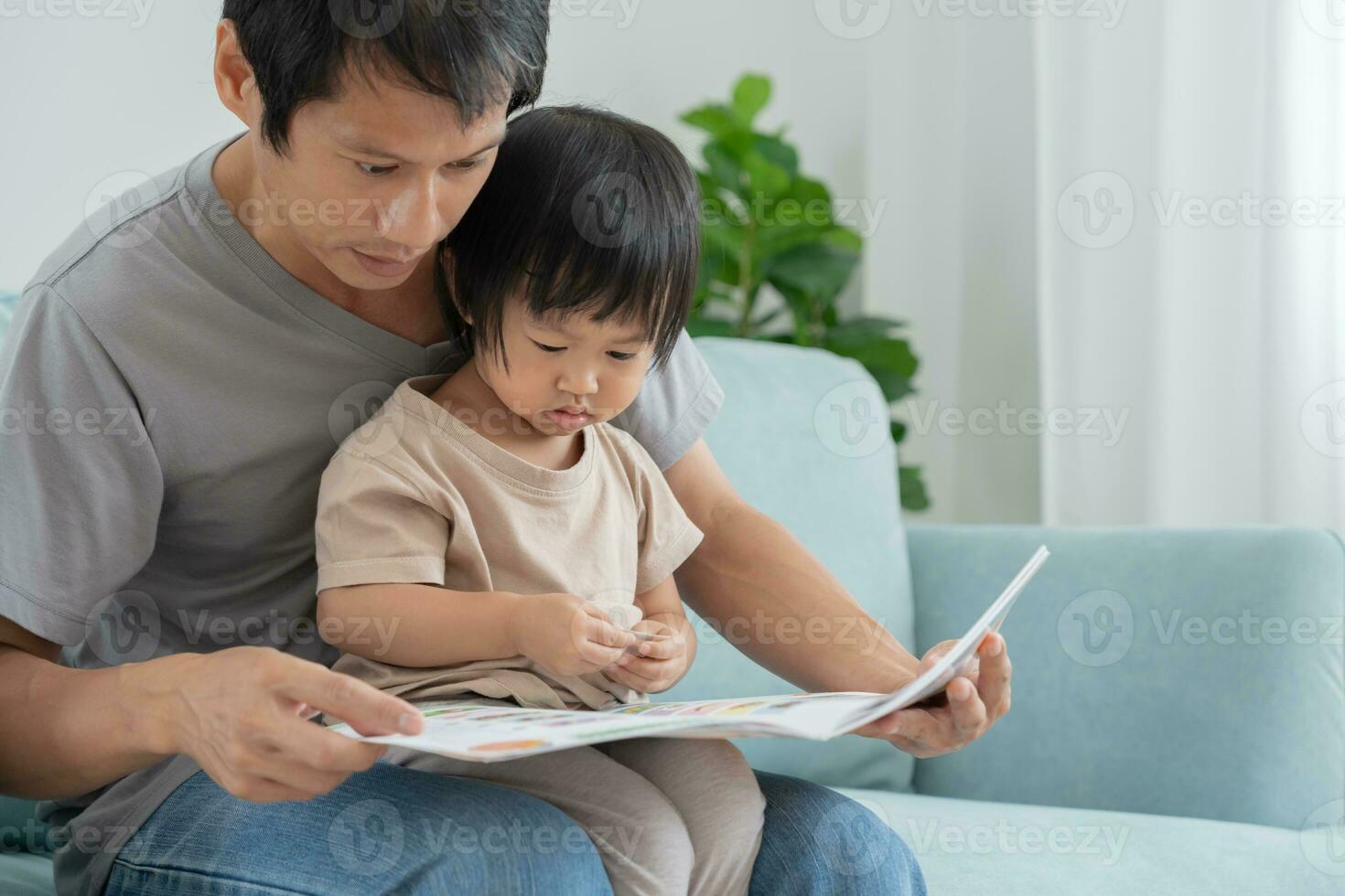 contento asiatico padre rilassare e leggere libro con bambino tempo insieme a casa. genitore sedersi su divano con figlia e lettura un' storia. imparare sviluppo, assistenza all'infanzia, ridendo, formazione scolastica, narrativa, la pratica. foto