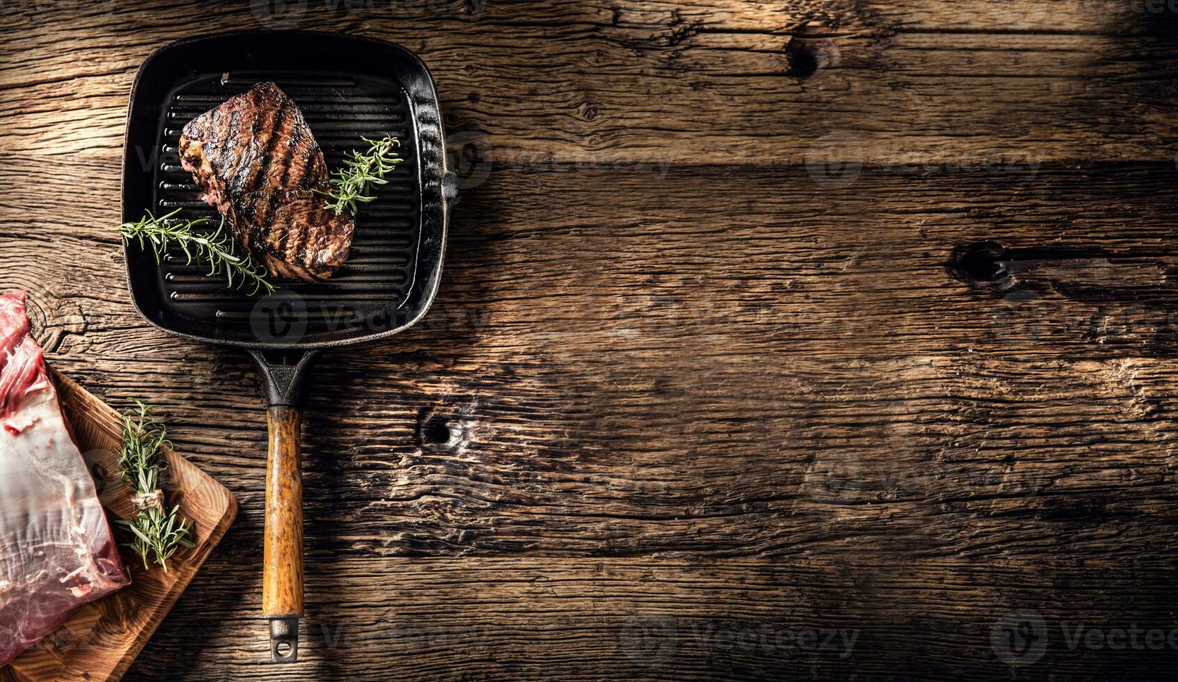 grigliato Manzo bistecca nel griglia padella con erbe aromatiche rosmarino su di legno tavolo foto