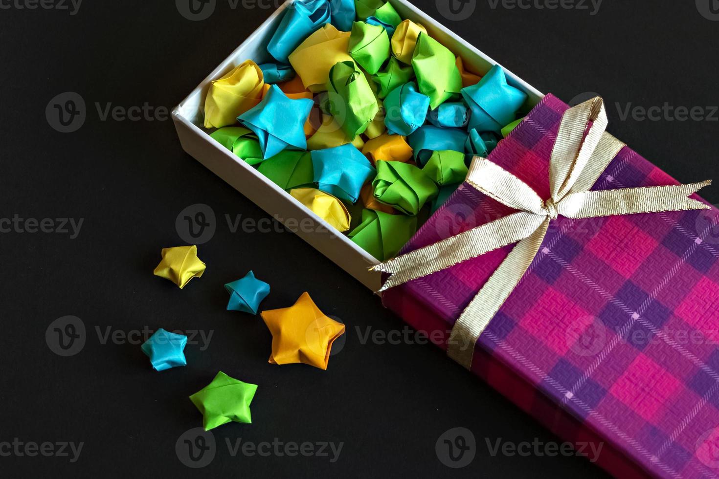 confezione regalo colorata con fiocco in raso con stelle di carta origami su sfondo nero foto