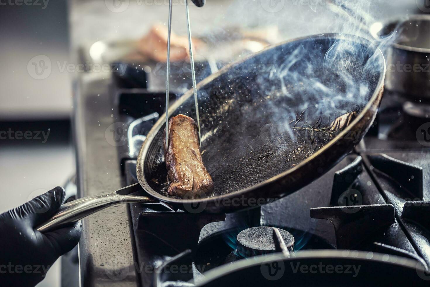 dettaglio di un' padella con aglio e rosmarino Appoggiato per un' lato nel ordine per raccogliere un' pezzo di carne con pinzetta foto