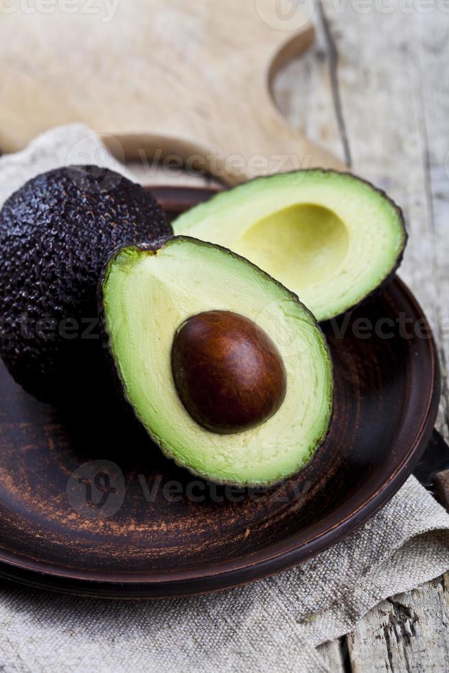 Avocado organico fresco sul piatto di ceramica e tovagliolo di lino sul fondo della tavola in legno rustico. foto