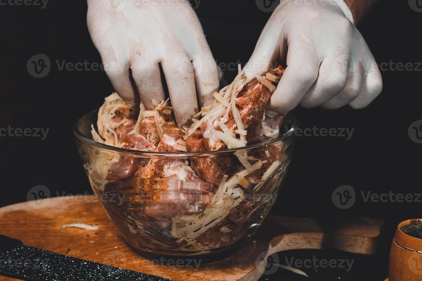 marinatura di maiale crudo per la cottura di spiedini e prosciutto. lo chef del ristorante in guanti tratta la carne con basilico e spezie al curry. foto