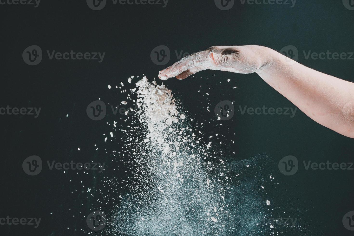 isolato su sfondo nero la mano femminile versa la farina bianca come la neve per la cottura foto