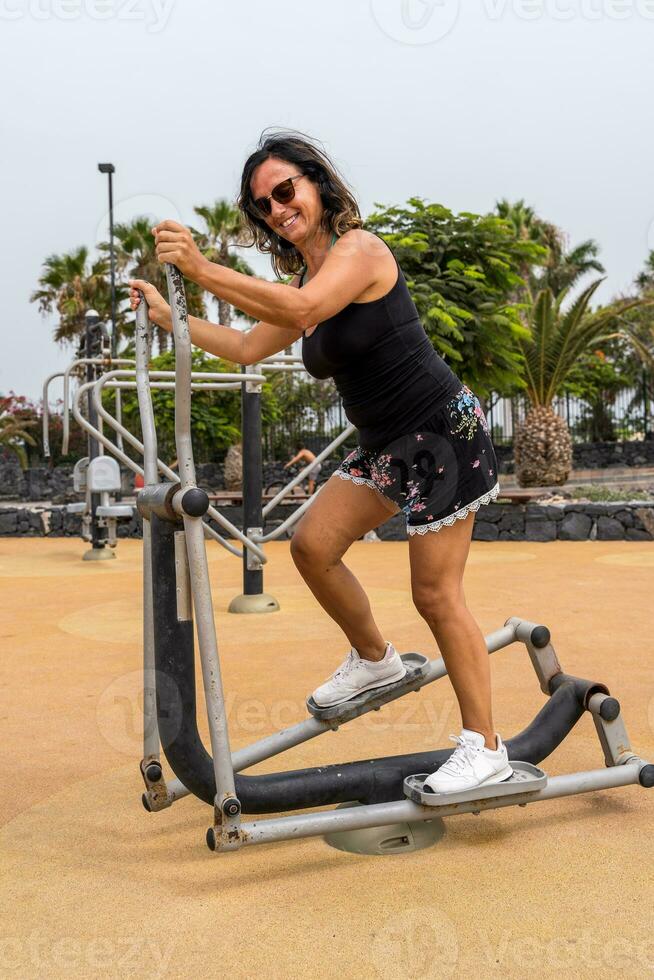 attraente mezzo anziano donna fare ginnastica esercizi nel un all'aperto pubblico Palestra a un' ricorrere foto