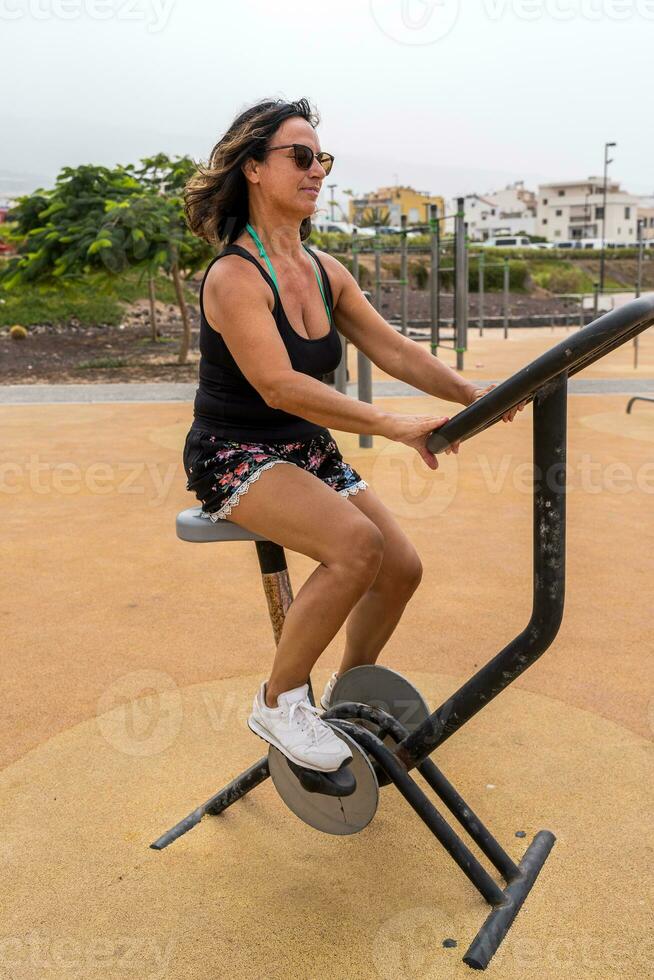 attraente mezzo anziano donna fare ginnastica esercizi nel un all'aperto pubblico Palestra a un' ricorrere foto