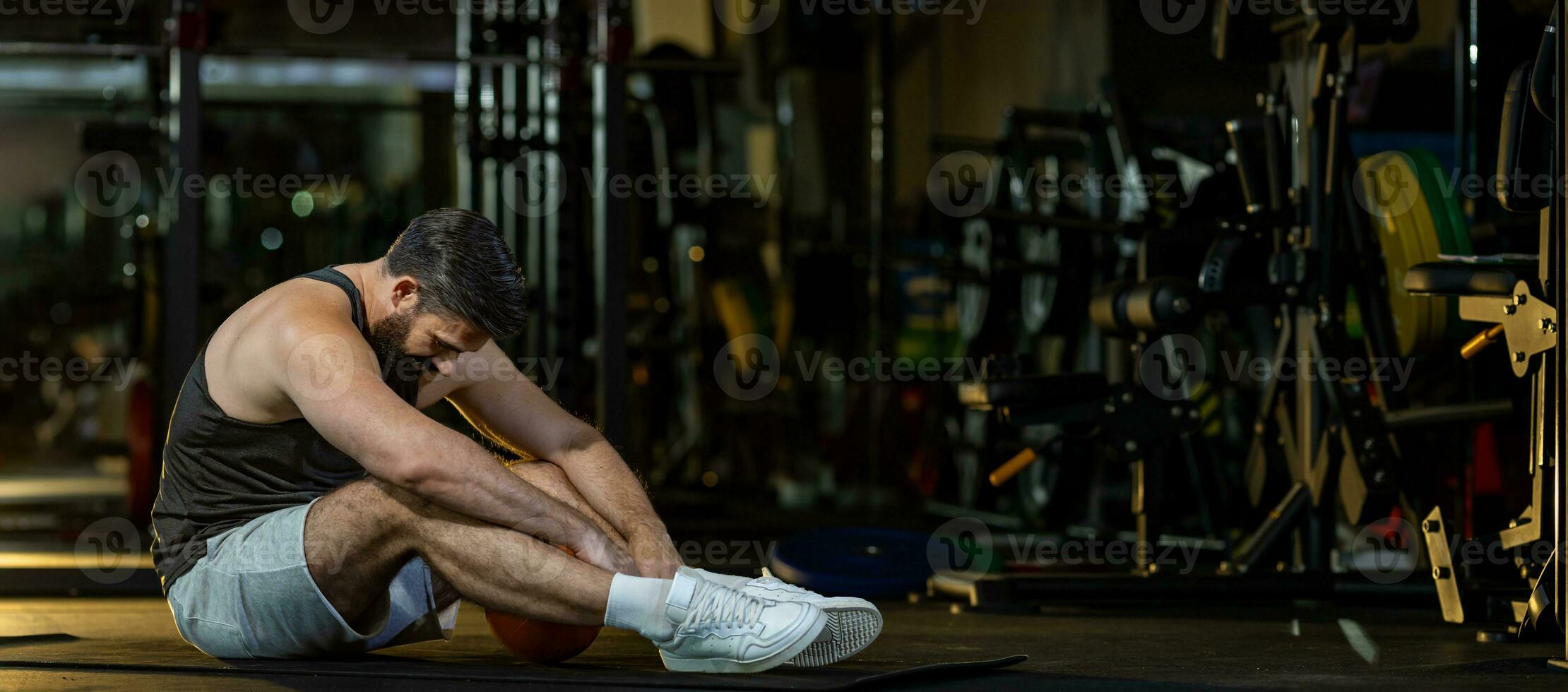 caucasico uomo è di fronte sovrallenamento sindrome dopo allenarsi dentro Palestra con buio sfondo per esercizio e fitness concetto foto