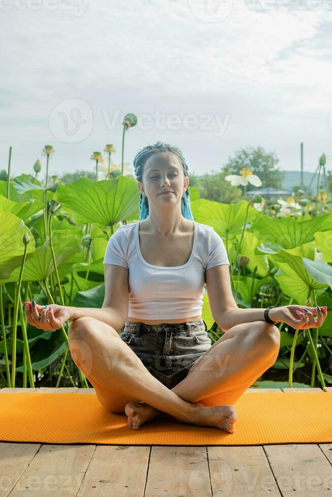 giovane donna con bellissimo blu dreadlocks riposo su yoga stuoia su loto lago foto