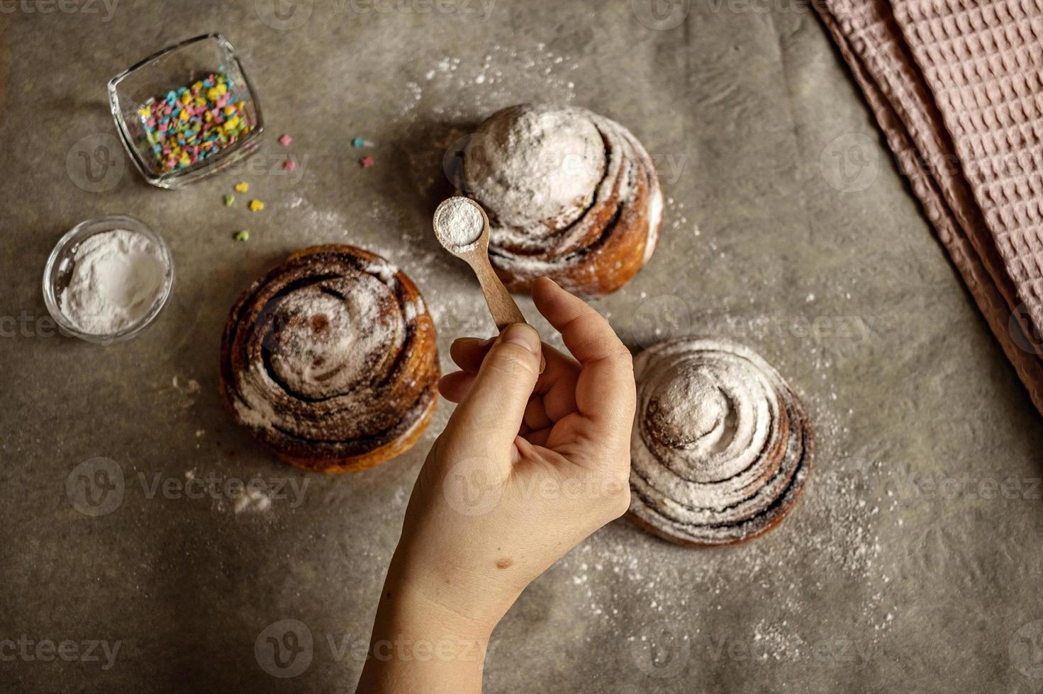 la mano della donna cosparge lo zucchero a velo sui panini alla cannella appena sfornati foto