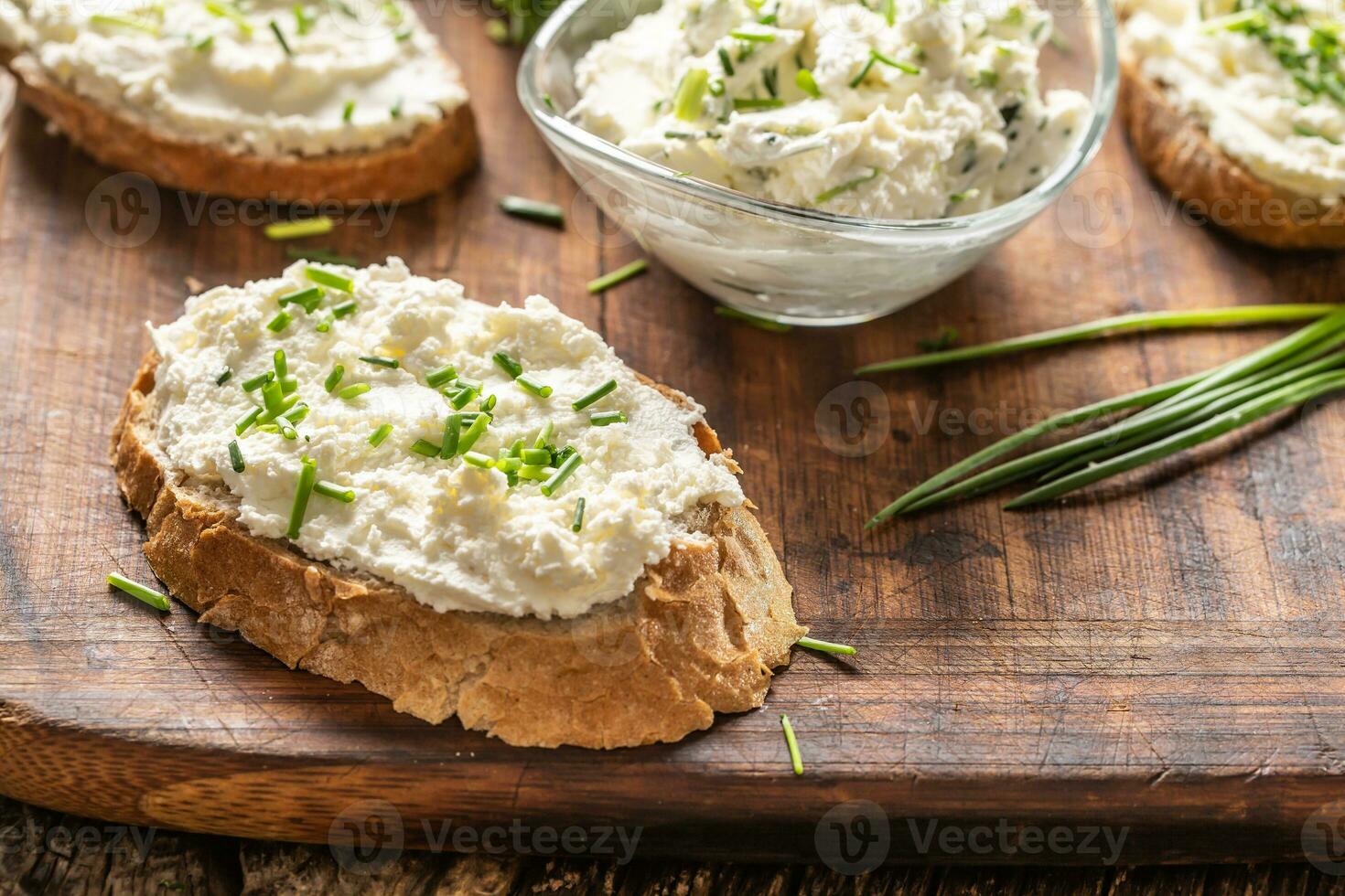 fette di croccante pane e un' bicchiere ciotola con un' crema formaggio diffusione e tagliare erba cipollina su un' Vintage ▾ di legno taglio tavola foto