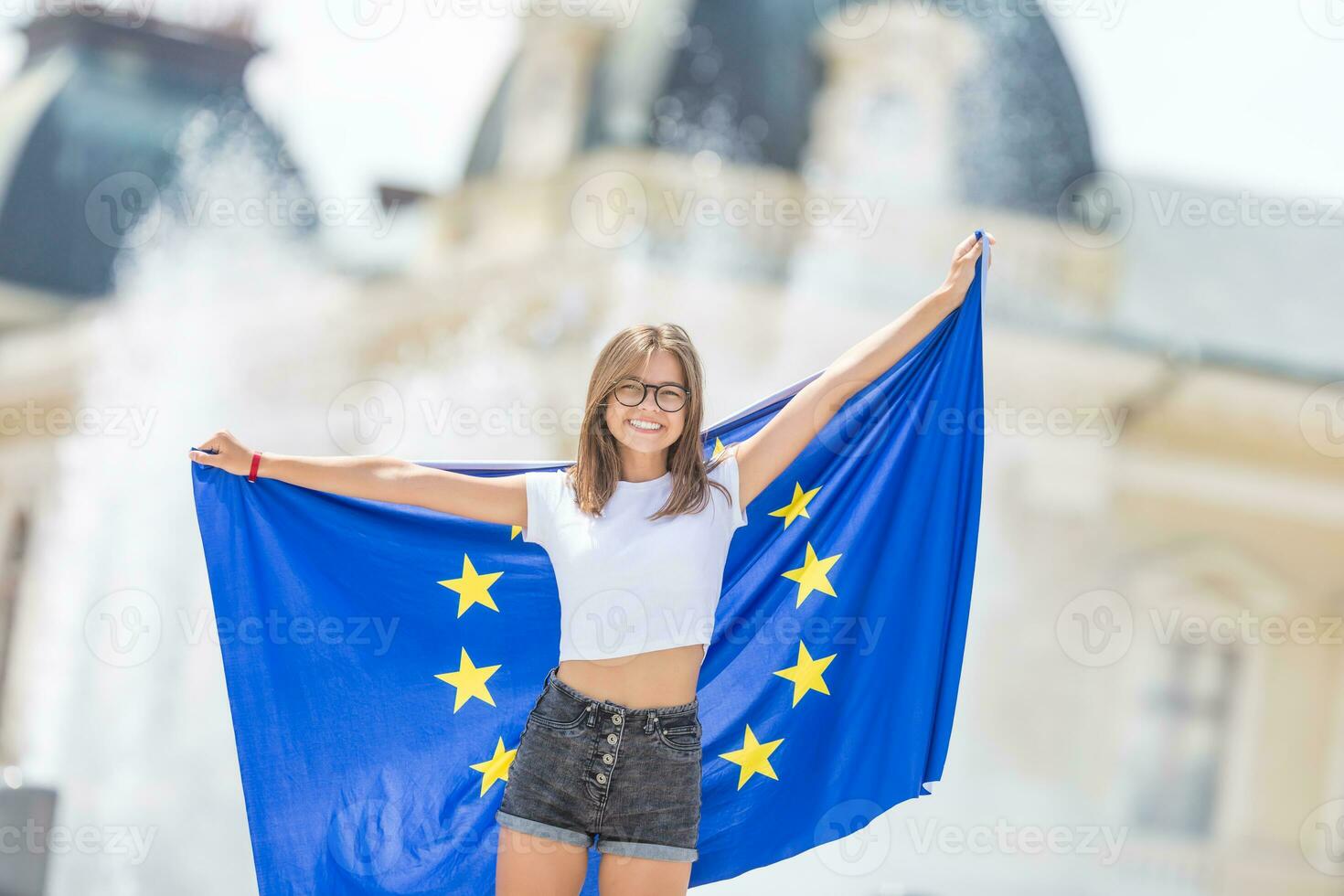 carino contento giovane ragazza con il bandiera di il europeo unione nel davanti di un' storico edificio da qualche parte nel Europa. foto