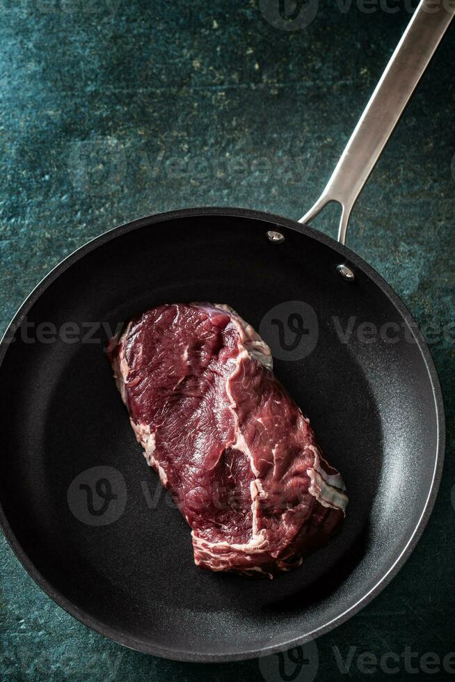 superiore Visualizza di un' buio padella con un' crudo pezzo di bistecca carne su un' marmo superficie foto